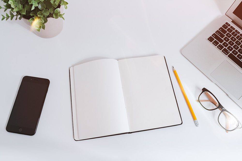 White desk with a smartphone, notebook, glasses and laptop